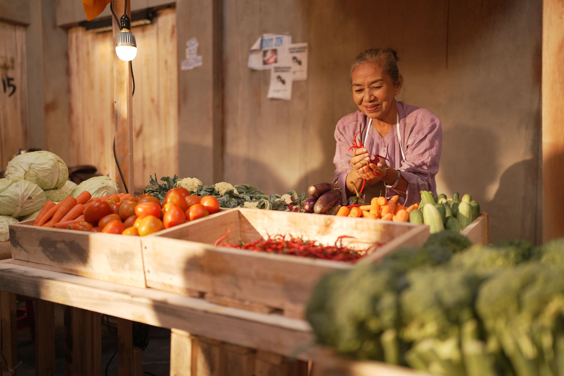 A produce manager at an outdoor market stand in warm morning light.